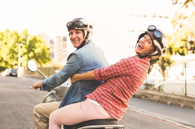 Happy mature couple riding a scooter in the city on a sunny day.jpeg